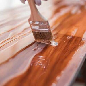 A person painting wooden furniture with brown paint.